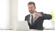 © stockbakers - Young Businessman Showing Thumbs Down Sign While using Laptop in Office