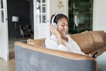 A woman audiobook at home listening to a playlist of music with headphones in the app