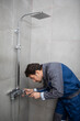 © Vitaliy - Handsome plumber fixing shower in the bathroom. Cheerful repairman standing and holding screwdriver in maintenance and service concept