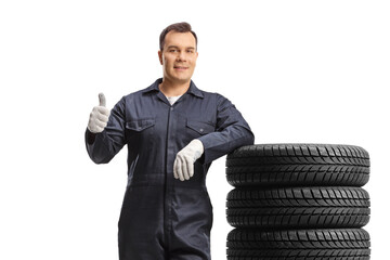 Wall Mural - Car mechanic in a uniform leaning on a pile of tires and showing a thumb up gesture