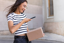 Smiling Female Courier Photographing Parcel On Street