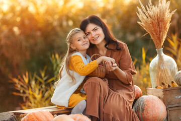 Mom and daughter at the sunset. Happy young mother hugging her daughter on sunshine warm autumn between pumpkins.