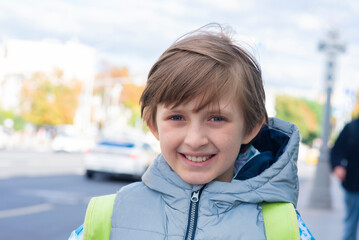 Wall Mural - portrait of a happy smiling schoolboy with a backpack on a windy day waiting for a bus near the road