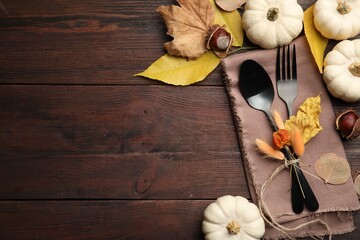 Seasonal table setting, space for text. Cutlery with pumpkins and autumn leaves on wooden background, flat lay