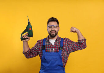 Wall Mural - Young worker in uniform with power drill on yellow background