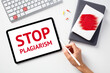Stop plagiarism concept. Office desk table with keyboard, paper notebooks, tablet. Message STOP PLAGIARISM on tablet screen.