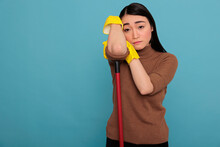 Overworked Stressed Asian Housekeeper Feeling Negative, Houseworker Takin Some Rest Wearing Yellow Gloves Holding On Brush Stick Isolated Against A Blue Background, Cleaning Home Concept,