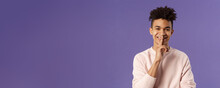 Close-up Portrait Of Attractive Smiling Young Man Hiding Secret, Asking Keep Silent Or Quiet To Do Surprise, Show Shush Gesture, Place Index Finger To Mouth, Standing Purple Background