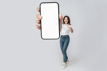 Full length of cheerful Asian woman smiling with showing cellphone blank screen with empty space for mobile app on screen. Isolated in studio pink background. Creative collage.