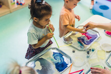 Multi-cultural Nursery School. Toddlers Playing With Striped Straws And Milk Painting, Using Nontoxic Food Coloring For Colors. Creative Kids Activity For Using Their Senses And Brain Development
