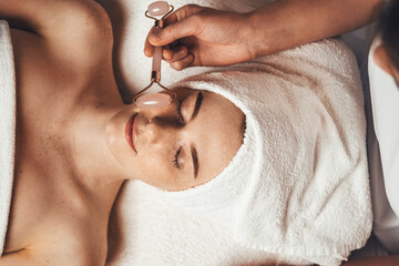 Wall Mural - close up portrait of beautician's hand massaging patient's face with jade roller at spa salon. beaut