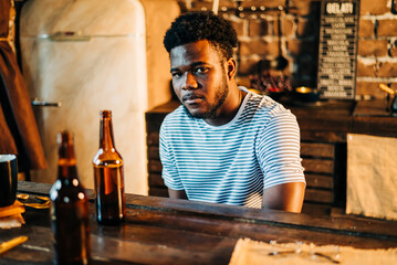 Shot of attractive african young happy smiling man drinking beer bottle in the bar close up portrait.