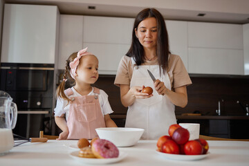 Wall Mural - A happy loving family is preparing a bakery together. Mother and daughter cook pancakes and have fun in the kitchen. Homemade food and a little helper