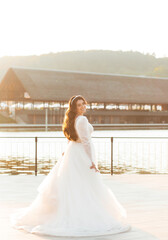 A beautiful bride in a white dress is circling the lake at sunset