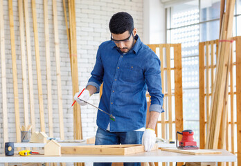 Wall Mural - Indian Asian professional engineer architect foreman labor worker wears safety goggles glasses and gloves using square angle degree ruler measuring wood on working table in housing construction site