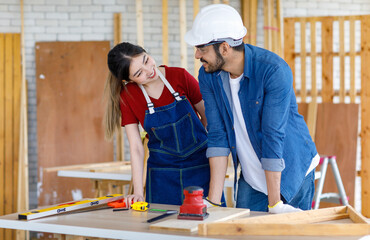 Wall Mural - Asian professional female and Indian bearded male engineer architect foreman labor worker lover couple wear safety hard helmet jeans apron and gloves standing smiling together in construction site