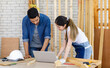 © Bangkok Click Studio - Asian professional cheerful female engineer architect foreman labor worker sitting smiling holding tablet computer discussing with Indian bearded male carpenter in workshop housing construction site