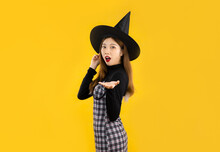 Halloween Costume, Asian Girl In Black Dress Wearing Witch Hat Hand Pointing On Yellow Background.