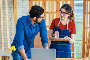 Wall Mural - Indian professional male engineer foreman labor worker using laptop computer meeting discussing with cheerful female colleague wear safety goggles writing note on paper clipboard in construction site