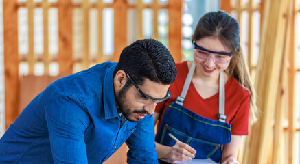 Wall Mural - Indian professional male engineer foreman labor worker using laptop computer meeting discussing with cheerful female colleague wear safety goggles writing note on paper clipboard in construction site