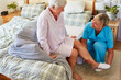 Pflegekraft hilft Seniorin beim Hausschuhe anziehen
