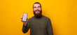 © Vulp - Handsome bearded man shows phone screen to the camera over yellow background.
