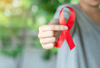 A young man show red ribbon on out of focus background.