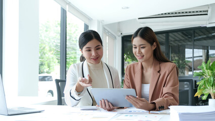 Two beautiful young asian businesswoman working together using digital tablet at office.