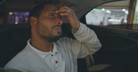 Upset young man covering face in anxiety while riding taxi cab in the backseat of car. One anxious African American person feeling overwhelmed by modern pressure