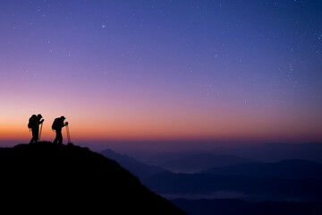 silhouette of two young hikers were standing at the top of the mountain looking at the stars and mil