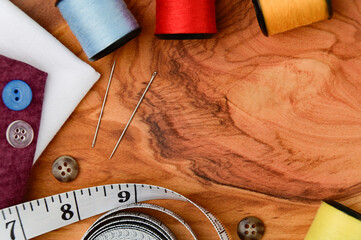 Sewing accessories and fabric on a wood background. Threads, needles, fabric, buttons and measuring tape. View from above top.