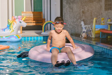 Cute Little Asian 6 Years Old School Boy Child In Swimming Goggles And Swimming Trunks Relaxing In An Inflatable Ring At Pool Villa In Summer Day, Happy Kid Having Fun On Summer Vacation