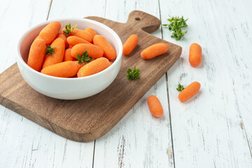 Baby carrots in a bowl over wooden table with herbs and copy space