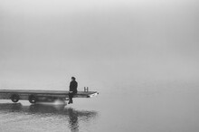 Young Woman Sitting On The River Dock In Winter Mist