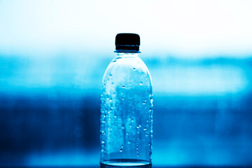 A plastic bottle with a black lid half filled with clean water stands against the background of blue water. Plastic pollution of the ocean. Drinking water.