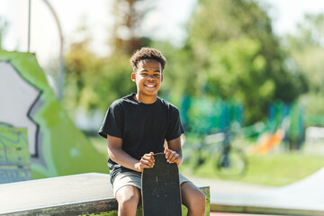 Afro-American boy with black t-shirt posing with his skateboard with the sky in the background