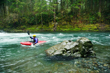 Side View Of Kayaker Paddling Through River In Forest