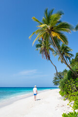 Wall Mural - young man walking along a tropical beach with palm trees