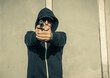 © bogdan vacarciuc - Man armed with a gun. The man is dressed in a hooded sweatshirt and wears a cap and sunglasses. Armed attack or self-defense - concept.