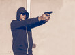 © bogdan vacarciuc - Armed attack or self-defense - concept. Man armed with a gun. The man is dressed in a hooded sweatshirt and wears a cap and sunglasses.