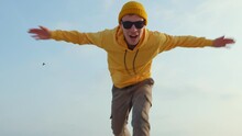 Running Man Blogger Caucasian Amusingly Moving His Hands With His Legs With Making Funny Faces On His Face Wearing Yellow Hoodie, Beanie Hat Sunglasses Close Up Blue Sky. Younger Generation. Lifestyle