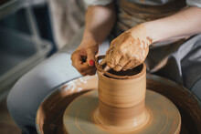 Midsection Of Female Potter Cutting Clay On Pottery Wheel With Thread At Workshop