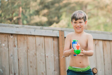 Happy Boy Playing With Squirt Gun While Standing By Wooden Fence At Yard