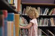 © Cavan Images - Side view of girl looking at book while standing in library