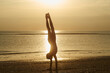 © Cavan Images - Full length of silhouette girl doing handstand at beach against sky during sunset