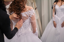 Side View Of Designer Assisting Bride In Trying Wedding Dress At Store