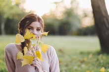 Portrait Of Young Woman Holding Leaves At Park During Autumn
