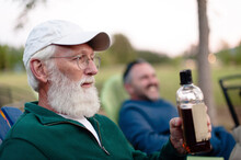Man Holding Bottle While Sitting With Friend In Yard