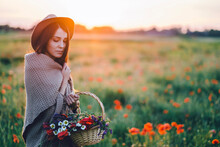 Woman Holding Flowers In Wicker Basket While Standing On Field Against Sky During Sunset