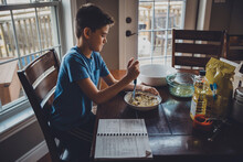 Side View Of Boy Mixing Muffin Ingredients In Bowl On Table At Home